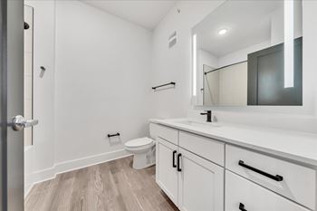 A white bathroom with a toilet, sink, and mirror at Luxe 360 on Centerpointe Apartments, Midlothian, Virginia